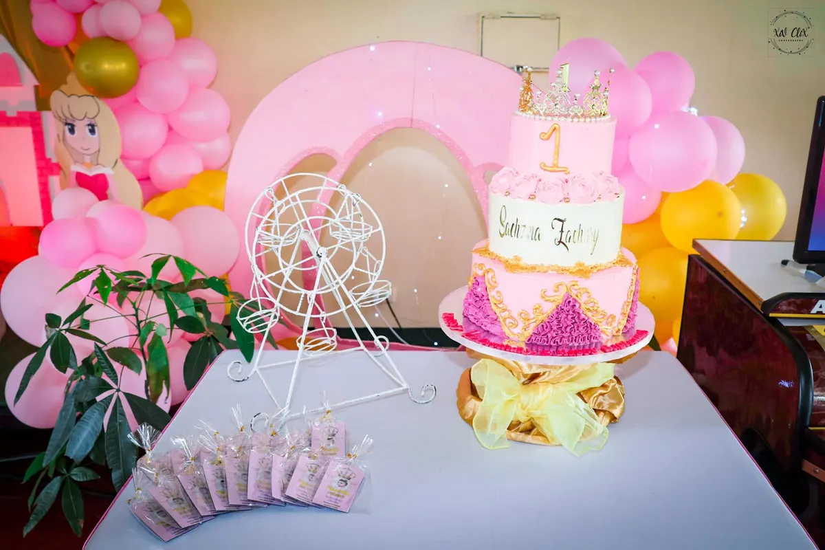 Two-tier pink christening cake with a carousel topper on a styled dessert table