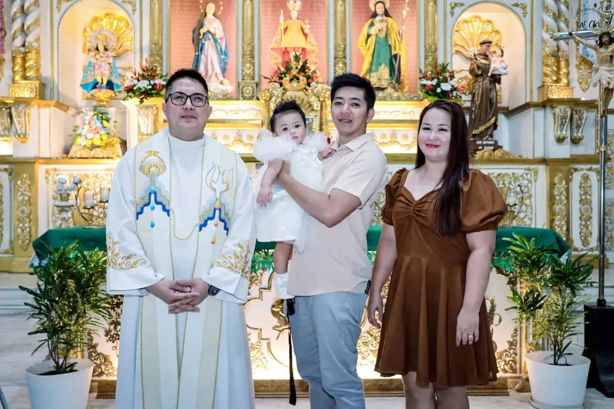 Parents holding their baby beside the priest in front of an ornate church altar