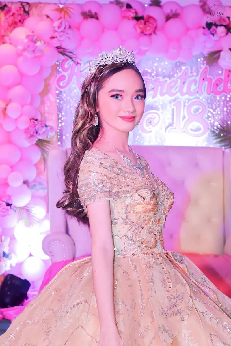 Debutante in a champagne gown in front of a pink balloon and floral backdrop