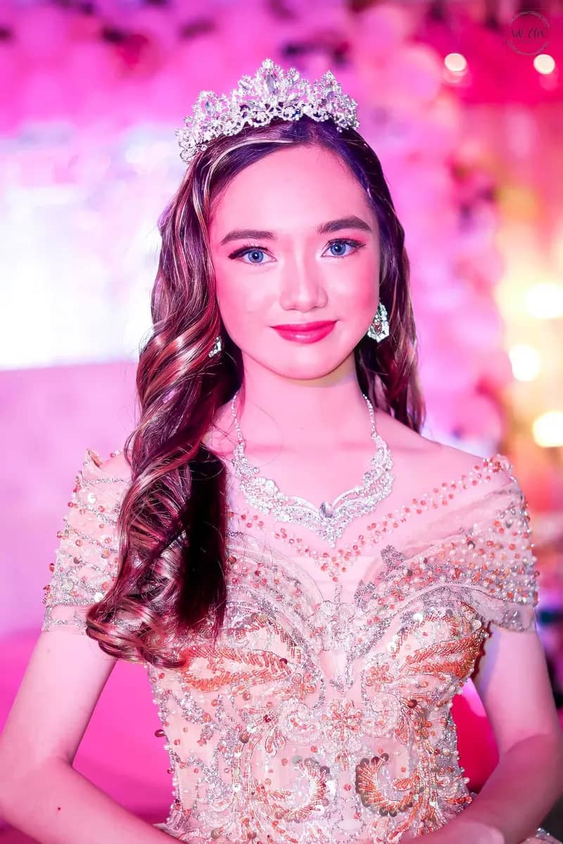 Debutante smiling in a tiara under bright pink stage lighting