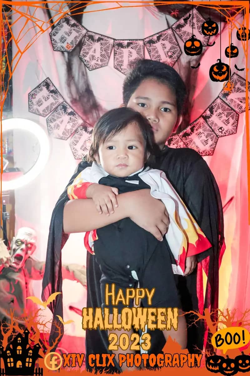Boy in a vampire cape holding a toddler at a Halloween photo booth