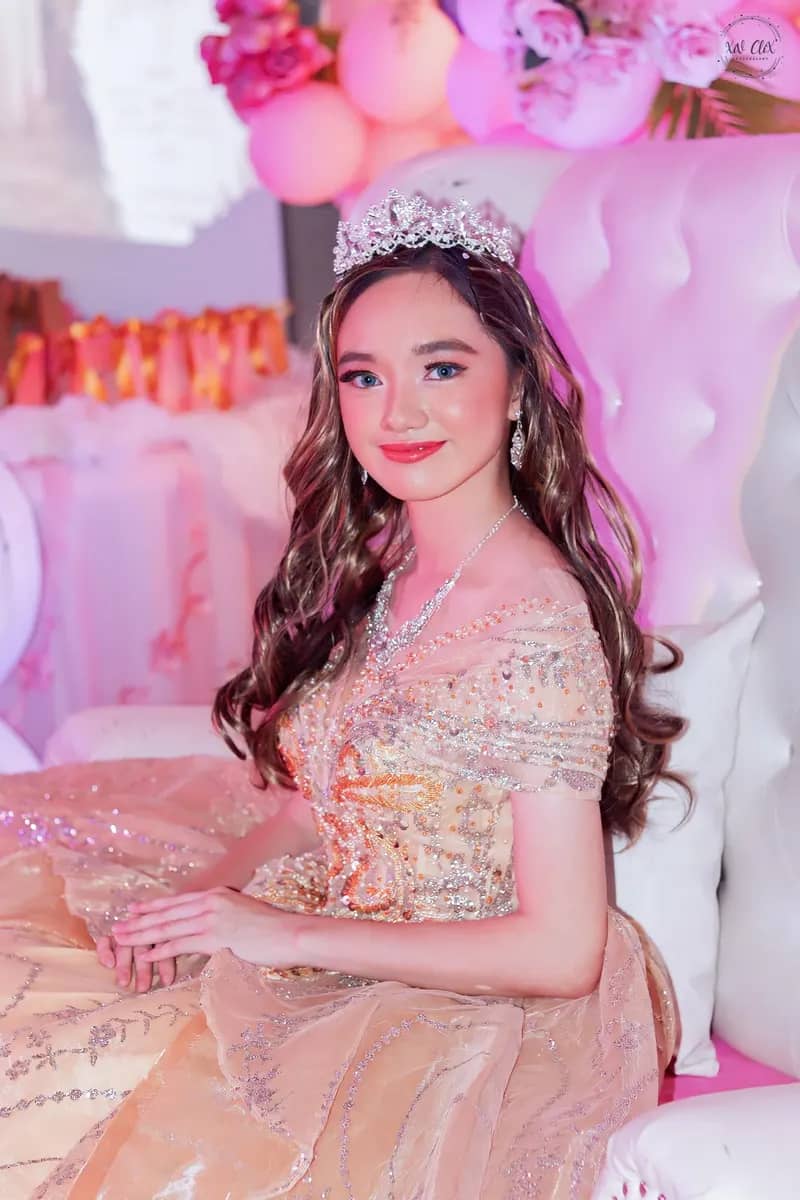 Debutante in a sparkling champagne gown and tiara seated on a white throne