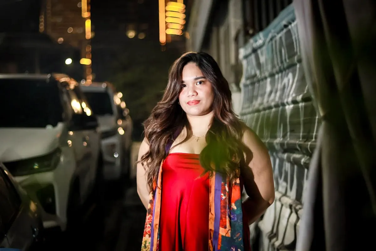 Woman in a red satin dress and patterned scarf posing on a city street at night